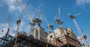 Multiple tower cranes operating at a large commercial construction site with partially completed high-rise buildings, illustrating modern construction scale and complexity.