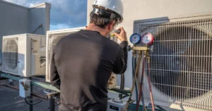 HVAC technician in safety gear servicing a rooftop commercial air conditioning unit with pressure gauges, ensuring optimal system performance and compliance with maintenance standards.