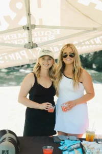 Two women smiling under a sponsor tent at Iron Mechanical’s Copper for Kids Annual Golf Tournament.