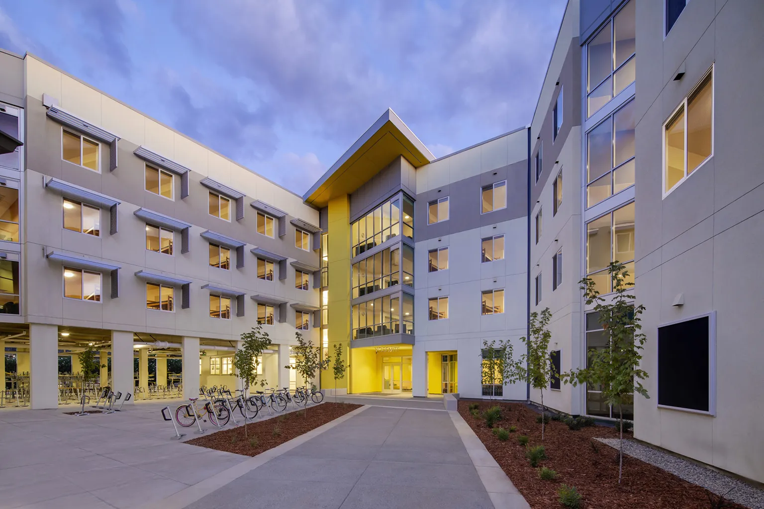 Modern multi-story building with a central courtyard, large windows, and warm lighting at dusk.