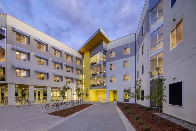 Modern multi-story building with a central courtyard, large windows, and warm lighting at dusk.