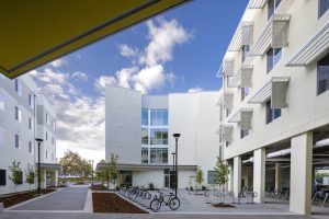 Modern courtyard surrounded by multi-story buildings with large windows, bike racks, and greenery.