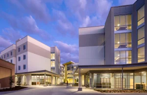 New Construction: Modern multi-story residential complex at dusk, with large glass windows and illuminated walkways.