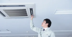HVAC technician inspecting a ceiling-mounted air conditioning unit to maintain indoor air quality and ensure proper airflow in a commercial building.