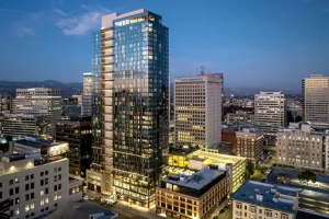 Modern high-rise residential tower in a city skyline at dusk, with illuminated windows and surrounding buildings.
