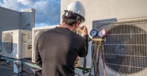 HVAC technician in safety gear checking refrigerant pressure on rooftop air conditioning units, illustrating professional commercial HVAC maintenance.