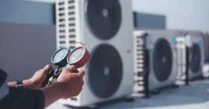 A technician uses a manifold gauge to inspect commercial HVAC units on a rooftop.