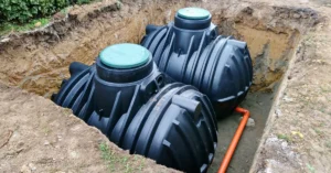 Underground black plastic water storage tanks being installed with visible orange piping, illustrating infrastructure for commercial water reservation or greywater reuse systems.