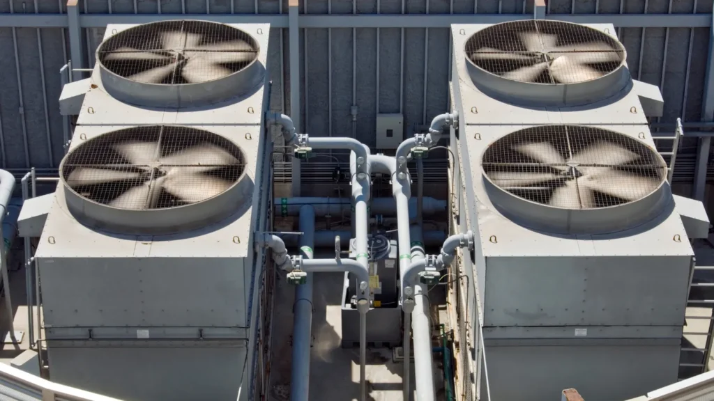 Top-down view of four large industrial HVAC cooling units with protective fan covers and interconnected piping, designed for high-capacity air conditioning in commercial or institutional buildings.