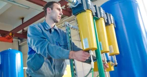 HVAC technician performing maintenance on a hospital air filtration system, adjusting yellow inline filter units connected to pressurized tanks for clean and regulated airflow.