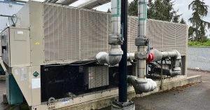 Large commercial chiller unit installed outside a healthcare facility, with insulated industrial-grade pipes transporting chilled water for HVAC climate control and medical equipment cooling.